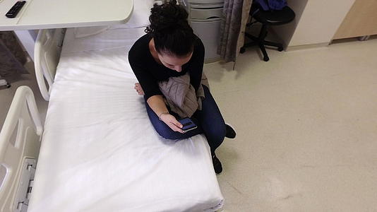女性患者在医院床上使用智能手机等待手术后出院视频的预览图
