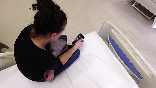 漂亮的女性患者用智能手机躺在医院床上手术后等待视频的预览图