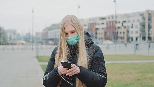 戴着医用口罩的年轻女性在街上看关于突发疾病的新闻视频的预览图
