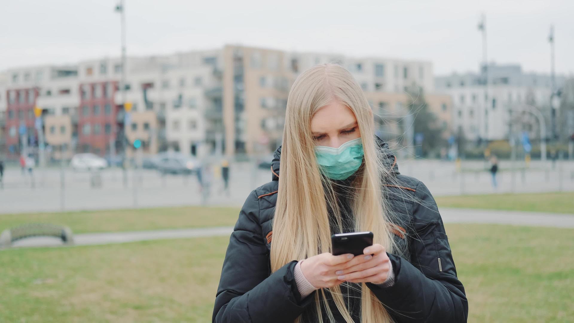 女性戴着医用面具阅读关于街上科罗纳突发疾病的新闻视频的预览图