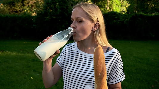 一位穿着牛仔裤和脱衣T恤的年轻女子在玻璃瓶里喝牛奶视频的预览图