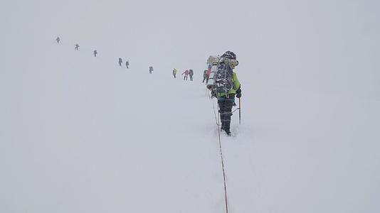 一群背着背包的登山者被绑在雪崩下雪山的冰川里视频的预览图