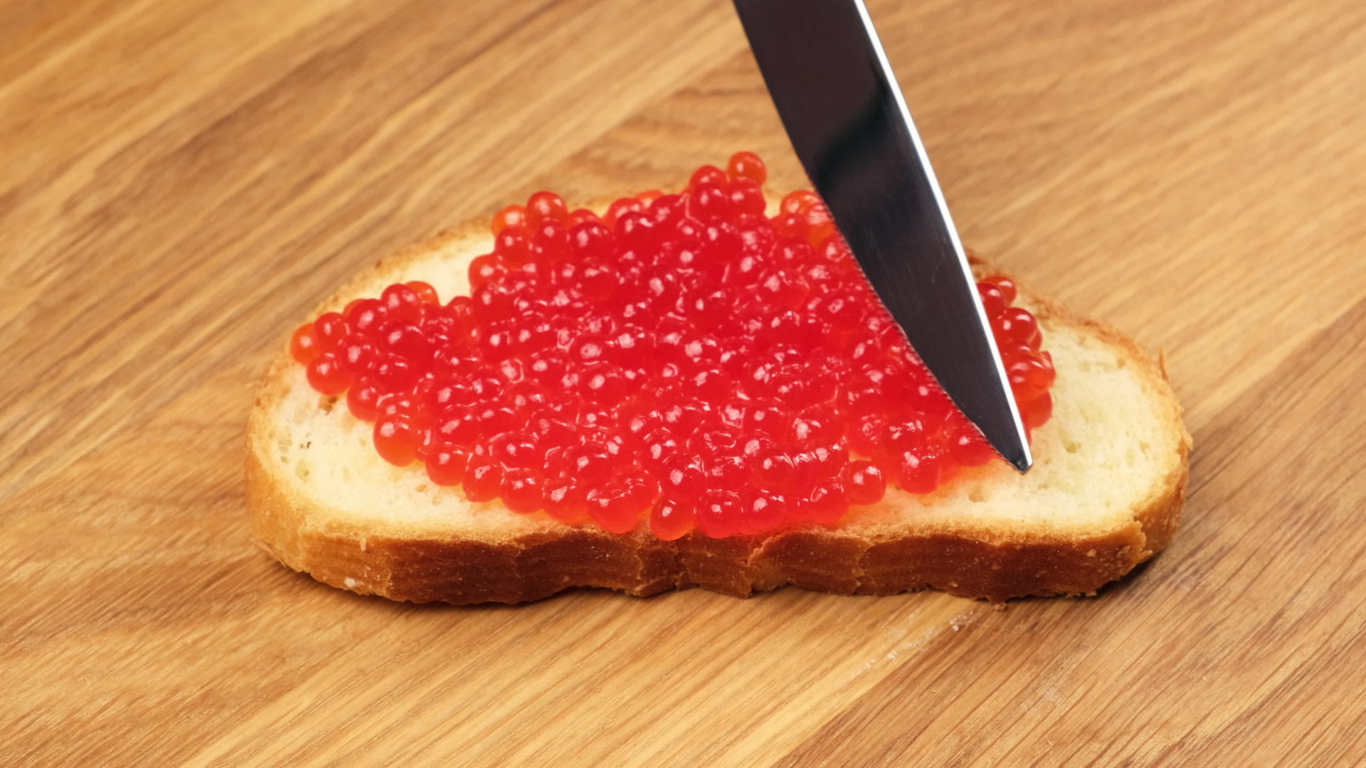 用刀在木桌上用白小麦粉做的面包上撒上刀红鲑鱼酱视频的预览图