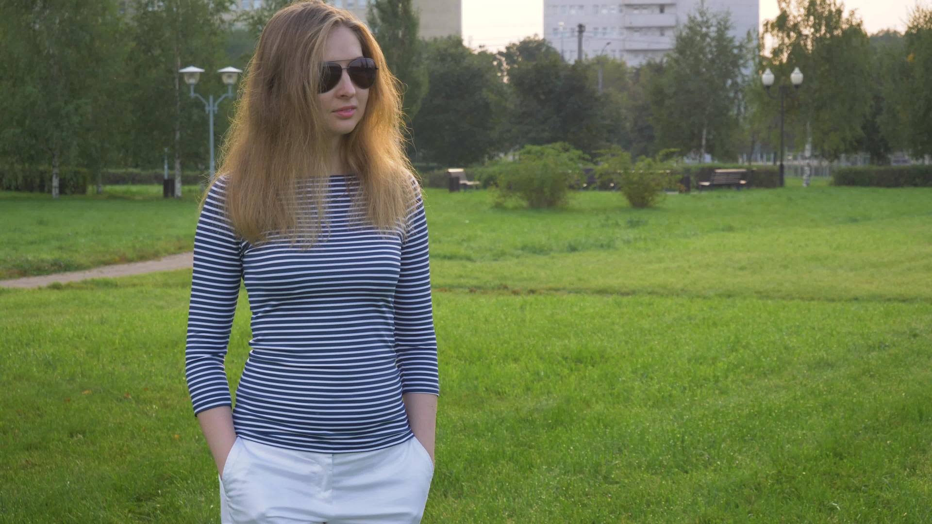戴着太阳镜长发的年轻女子在公园里走来走去视频的预览图