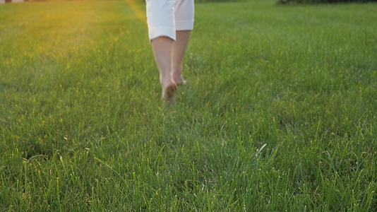 日落时年轻的白人妇女穿着白色的衣服在绿草中从相机里跑出来视频的预览图