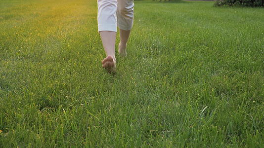 日落时年轻的白人妇女在绿草中跑向镜头赤脚双腿视频的预览图