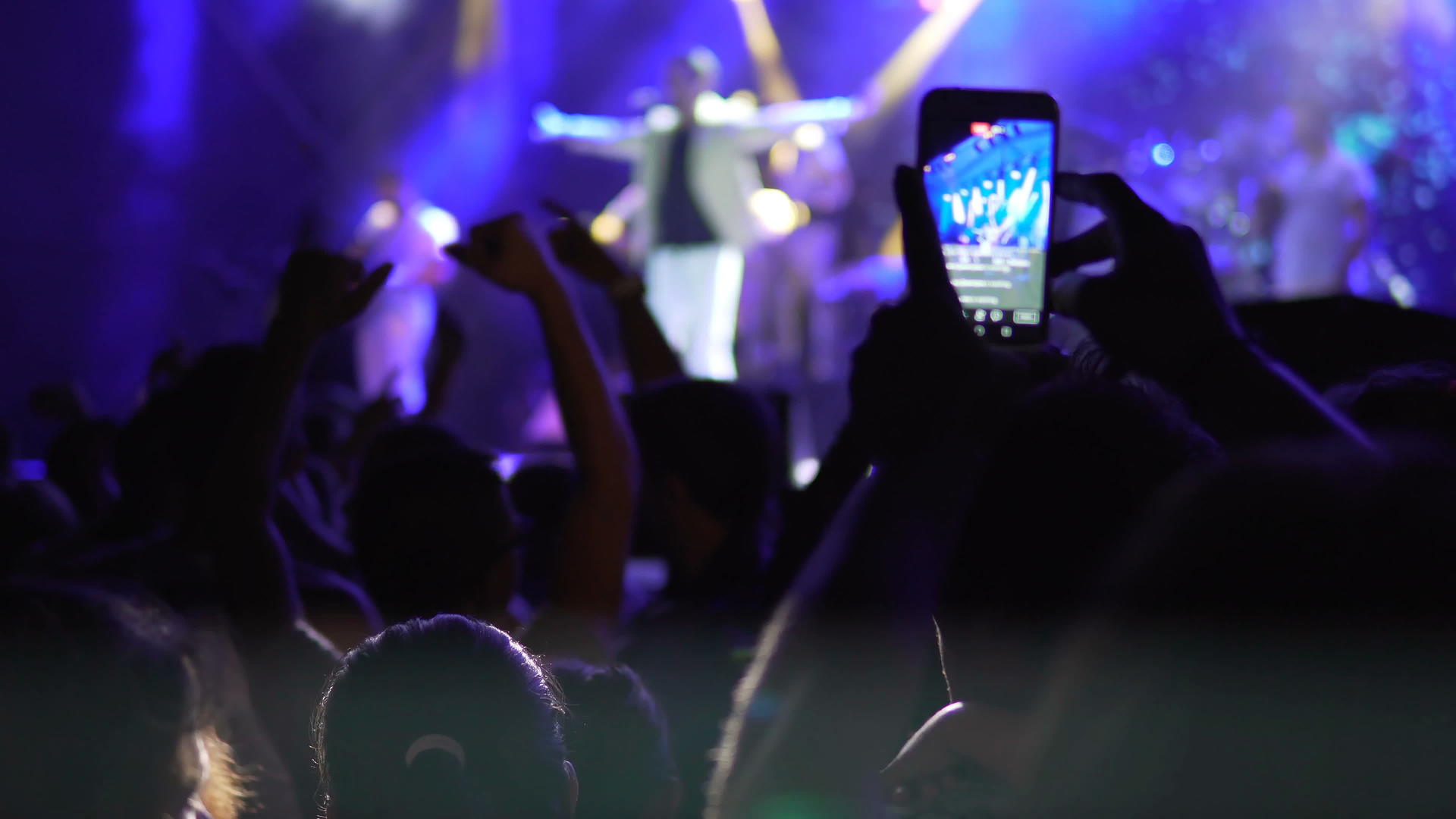 在音乐会上录制视频的手剪影包括灯光和烟雾以及许多人的流行音乐视频的预览图