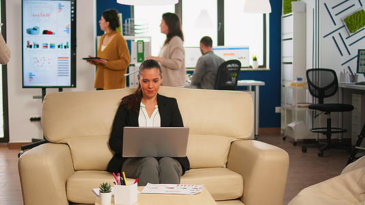 女经理拿着笔记本电脑坐在沙发上对着网络微笑视频的预览图