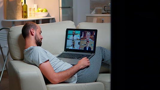 疲惫的男人穿着睡衣坐在沙发上和队友一起做网上生意视频的预览图