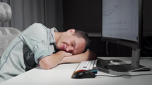 男人在睡梦中微笑在电脑前的桌子上休息视频的预览图