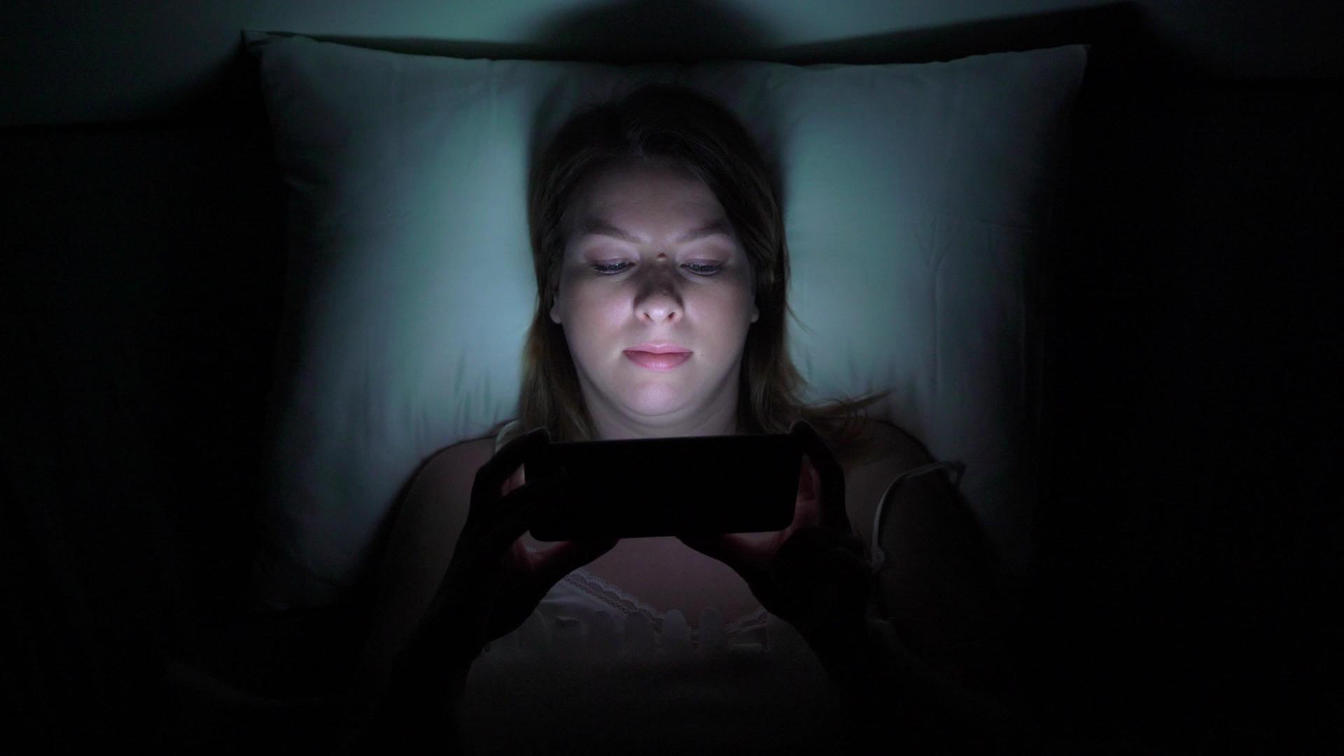 年轻女性晚上睡觉前用手机在床上移动成瘾者的概念视频的预览图