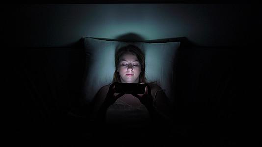 年轻女性晚上睡觉前用手机在床上移动成瘾者的概念视频的预览图