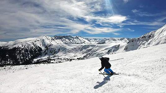 在阳光明媚的冬天在山里慢慢地看着高山滑雪者在山坡上滑雪视频的预览图