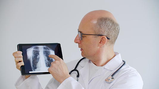 远程咨询时秃头医生在平板电脑屏幕上显示肺部x光视频的预览图