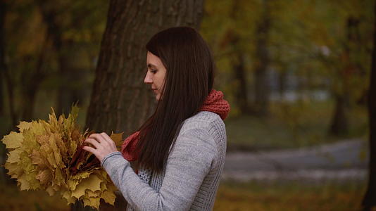 秋天女孩在公园里散步手里拿着树叶录像片被拍了下来视频的预览图