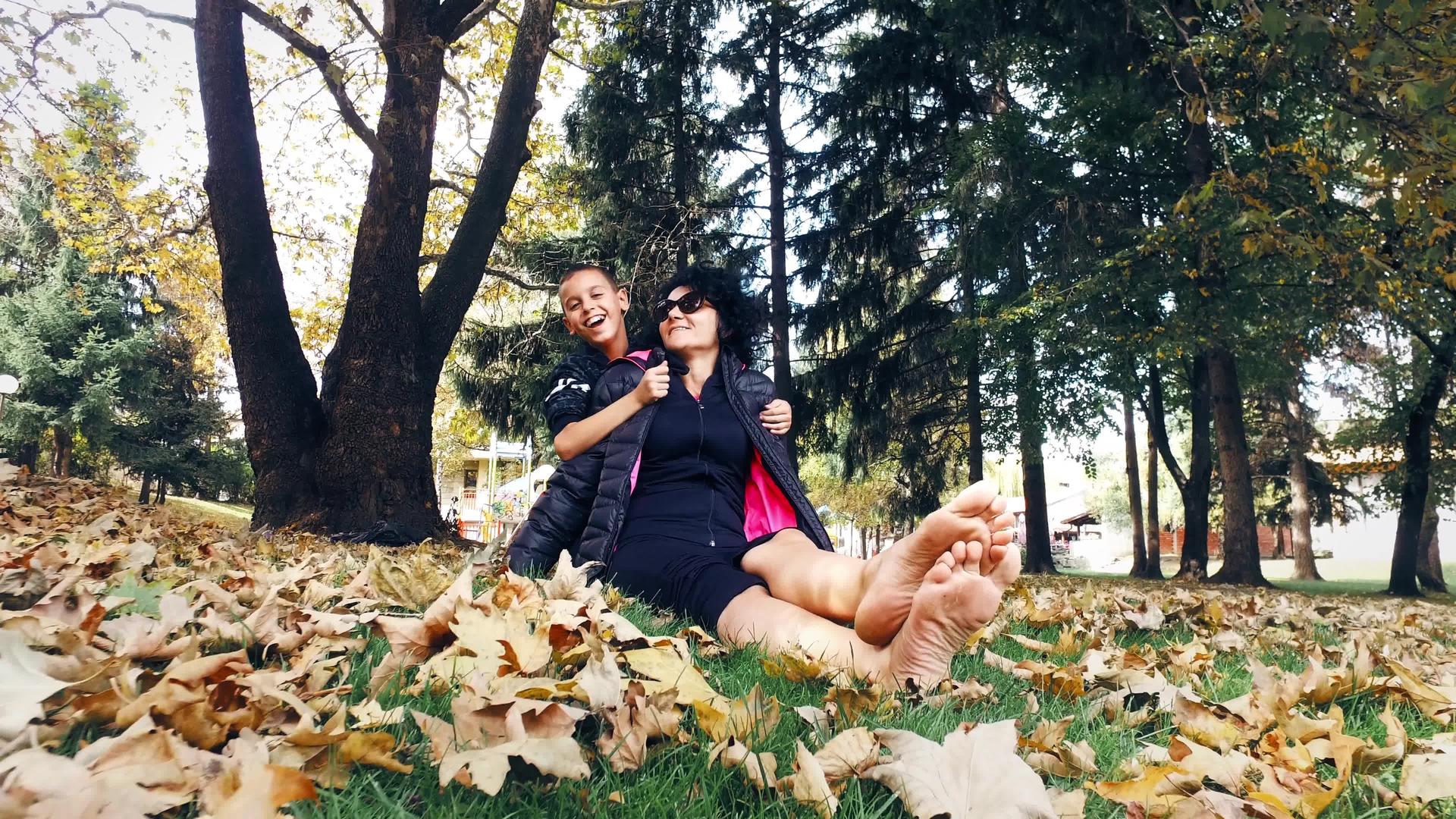 赤脚女女人和她的儿子在公园里玩得很开心用秋叶拥抱视频的预览图
