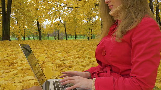 穿着红色斗篷的年轻白人妇女在膝盖电脑上打字视频的预览图