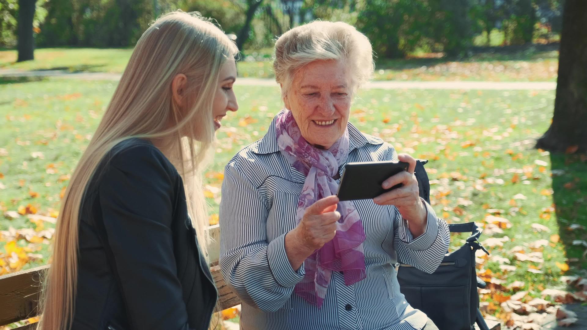 漂亮的金发女郎年长的女士坐在椅子上智能手机视频的预览图