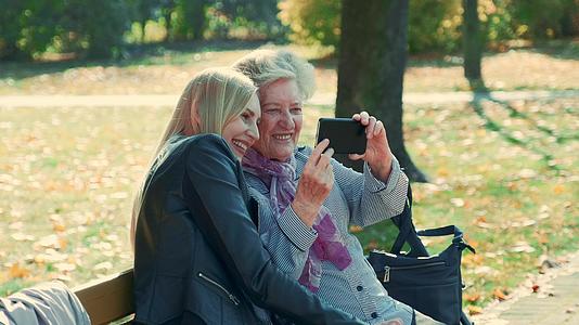 秋天年轻女性和老年女性在美丽的公园里用智能手机自拍视频的预览图
