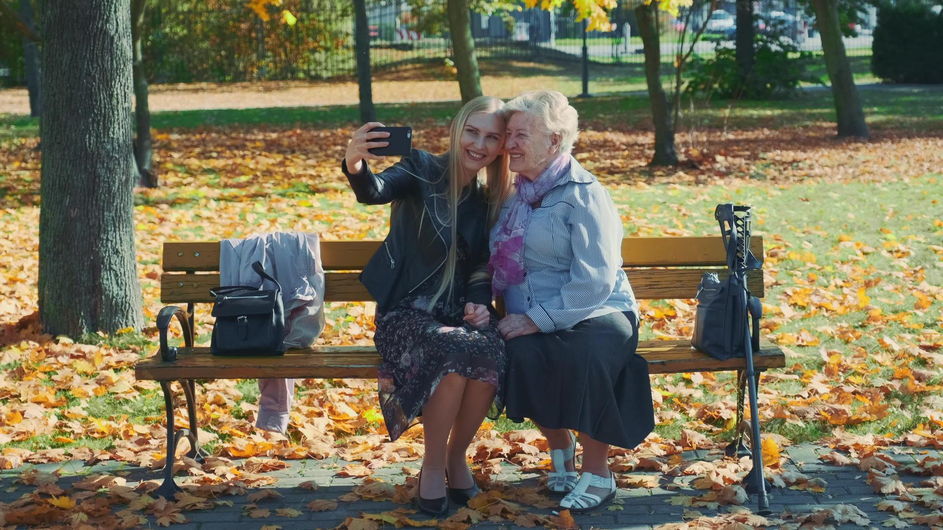 秋天年轻女性和老年女性在美丽的公园里用智能手机自拍视频的预览图