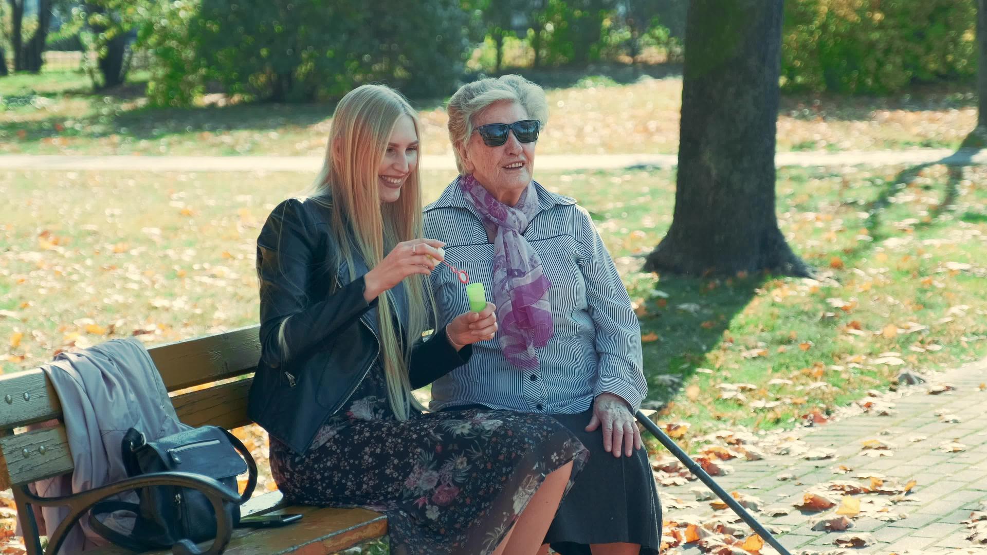 快乐的年轻女子和奶奶坐在公园里吹泡泡视频的预览图
