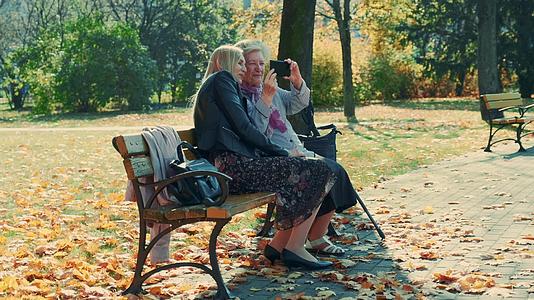 年轻女性和祖母在公园的智能手机上观看放大镜头视频的预览图