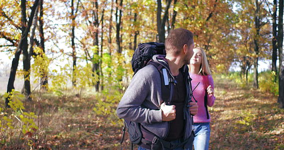 在一个阳光明媚的下午情侣们背着背包穿过秋天的森林看着两边视频的预览图