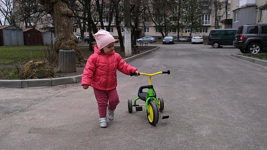 小女孩在三轮车旁边慢慢地走在街上视频的预览图