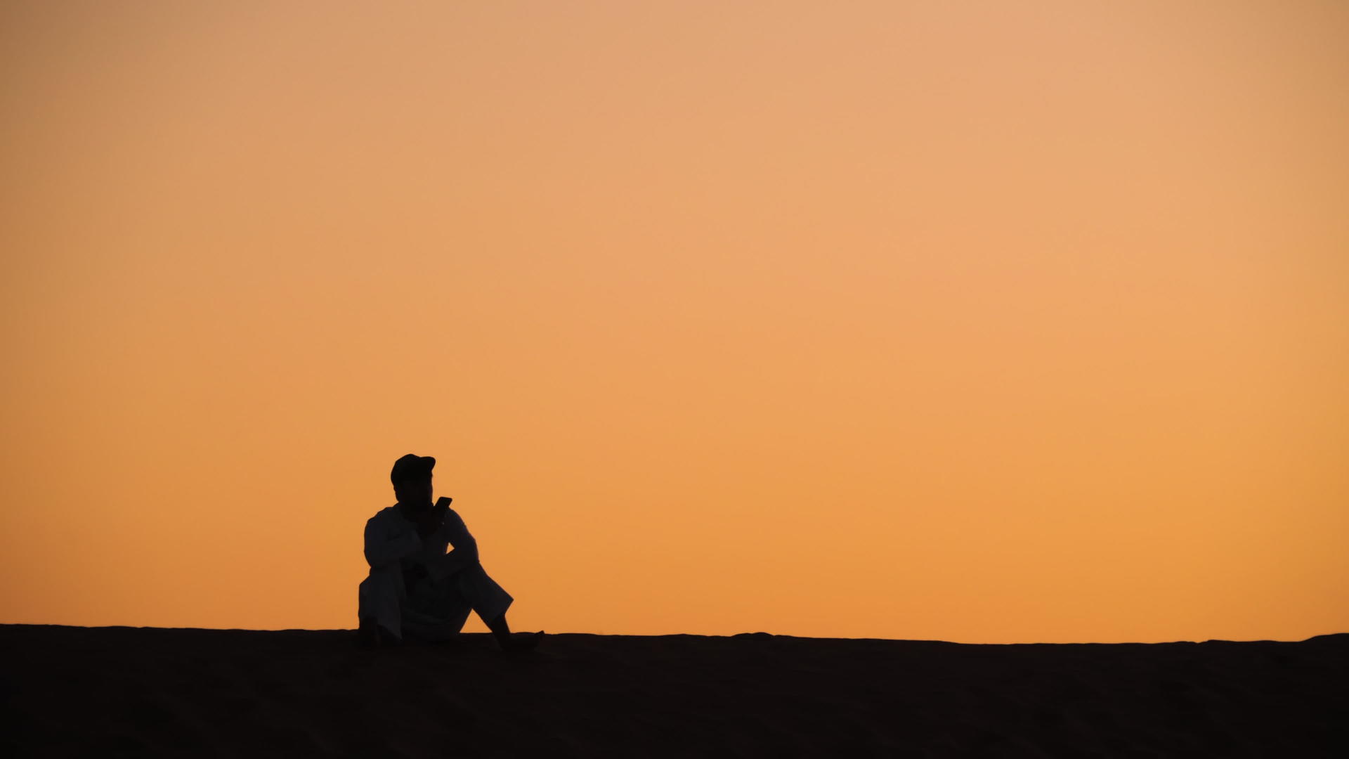 男人坐在沙丘上用手机说话视频的预览图