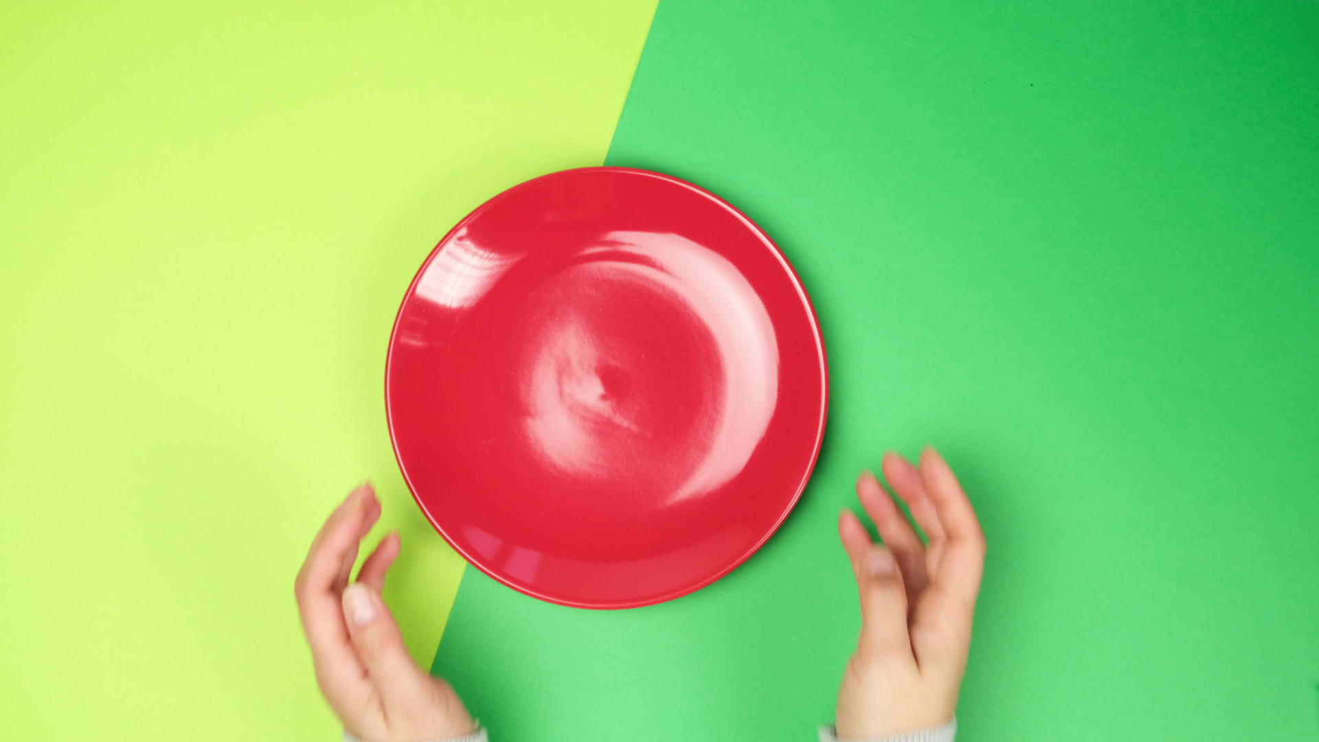 女人用手在绿色的表面上放一个空圆圆的红色陶瓷板的顶部视图视频的预览图