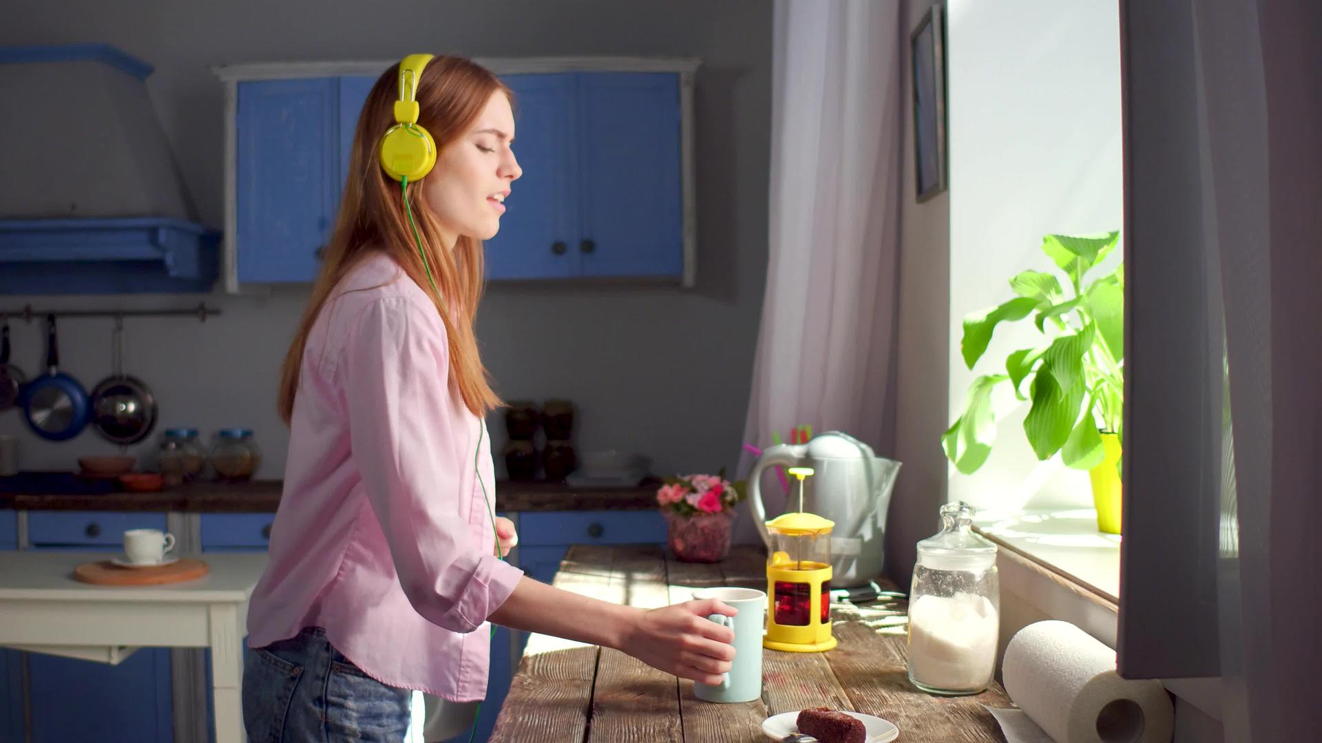 女孩在厨房喝茶在耳机里听音乐视频的预览图