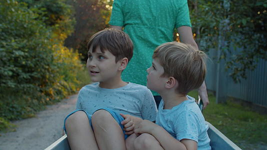 单亲妈妈和两个孩子坐在乡村街道上的手推车上视频的预览图