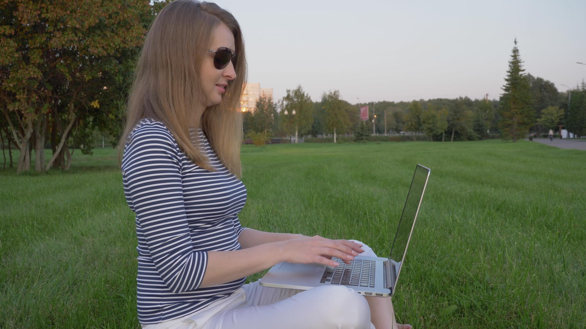 坐在草坪上在绿色城市公园里做笔记本电脑工作视频的预览图