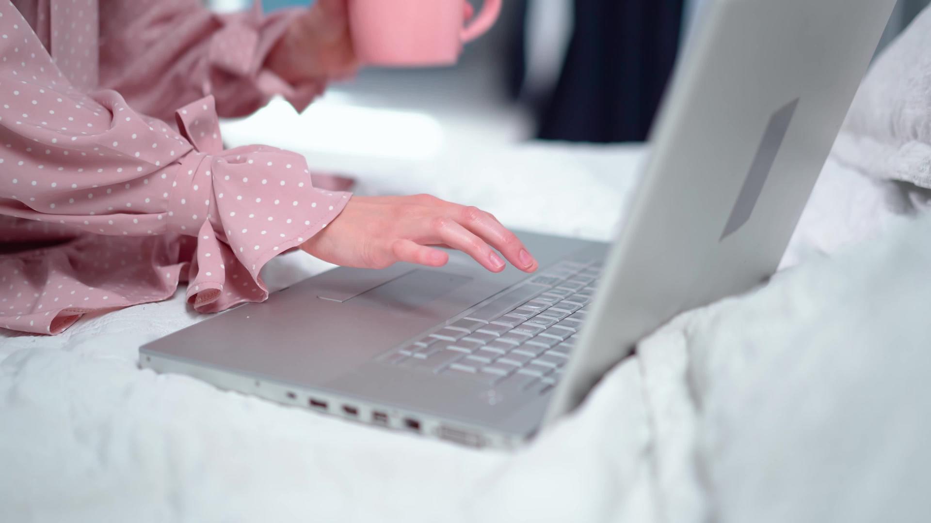坐在床上穿着粉红色的裙子在笔记本电脑上工作视频的预览图
