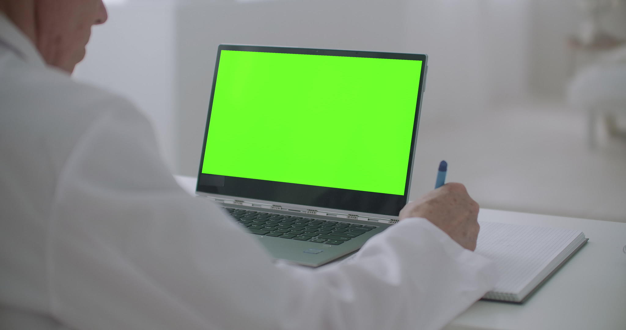 医生正在看笔记本电脑在诊所的办公桌上用绿屏检查笔记本电脑视频的预览图