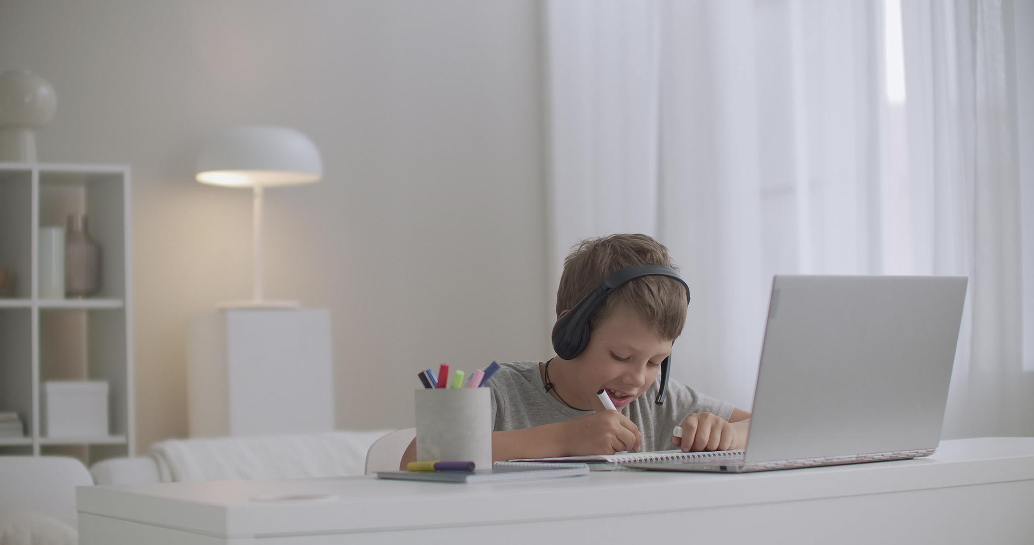 当代男孩在客厅里用笔记本电脑和耳机画纸视频的预览图