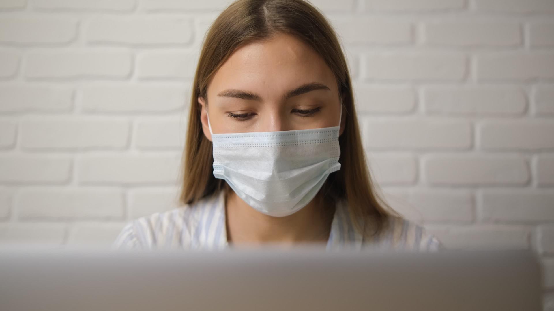 戴着医用面具和脱衣睡衣的女孩在笔记本电脑上远程工作视频的预览图