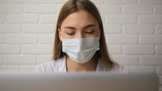 戴着医用面具和脱衣睡衣的女孩在笔记本电脑上远程工作视频的预览图