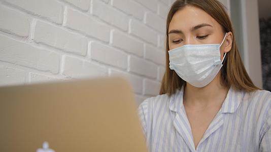 一个女孩戴着医用面具和脱衣睡衣远程工作笔记本电脑视频的预览图