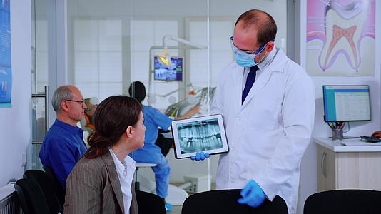 口腔科学家指向数字屏幕上向女性解释X射线视频的预览图