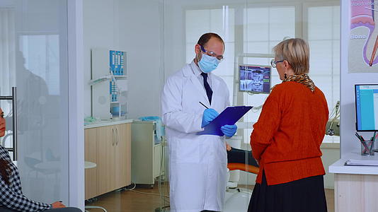 在等候区与老年妇女交谈时戴口罩的正畸牙医视频的预览图