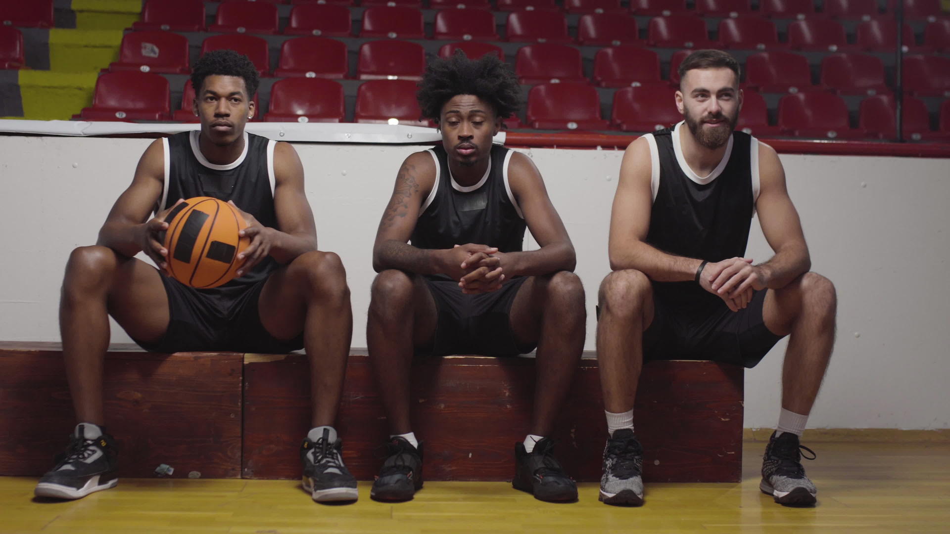三名篮球运动员坐在长凳上观看比赛视频的预览图