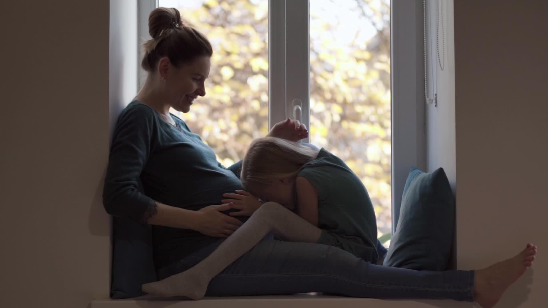 绿松石的年轻孕妇和小女孩的女儿在窗台上玩耍视频的预览图