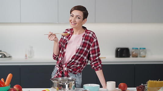 留着短发的性感家庭主妇在现代厨房里拿着一把长木勺视频的预览图