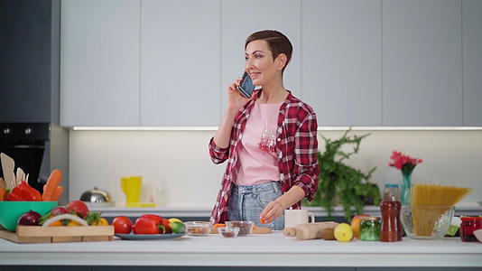 打电话给一个留着短发的漂亮女人吃胡萝卜在厨房准备食物呆在家里视频的预览图