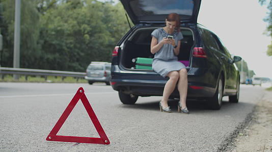 一位30多岁的年轻女子穿着裙子坐在汽车后备箱里用手机求助视频的预览图