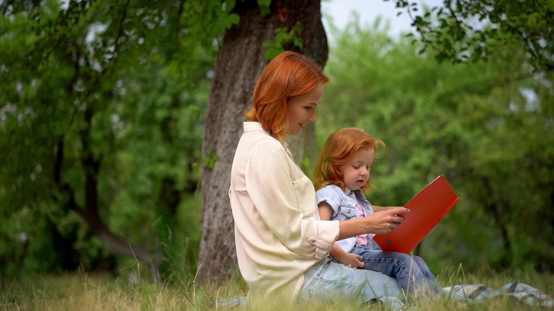 快乐的年轻母亲和女儿在户外阅读视频的预览图