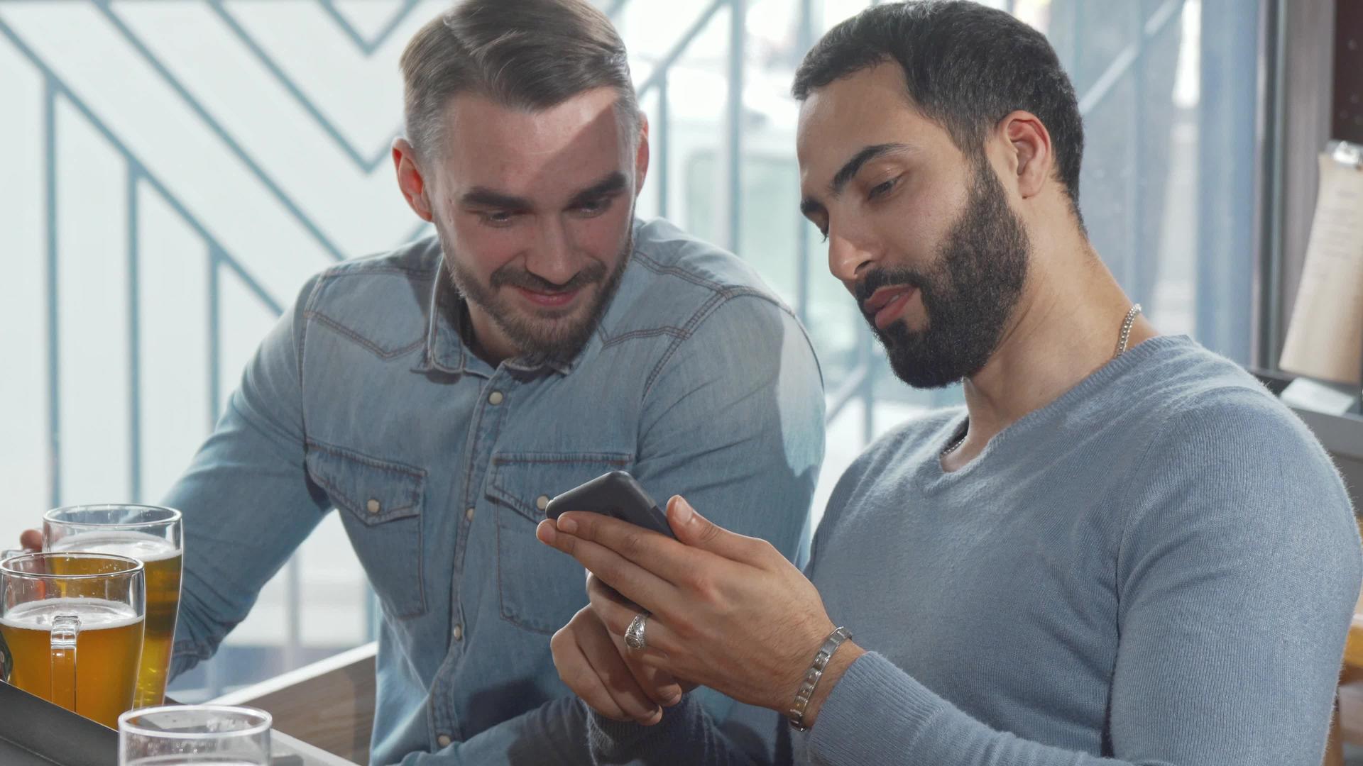 喝啤酒时两个男性朋友用智能手机喝啤酒视频的预览图