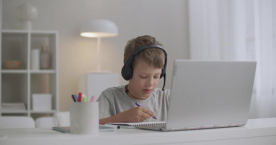 周末小男孩用耳机在家里用毡笔画画和学习音频视频的预览图