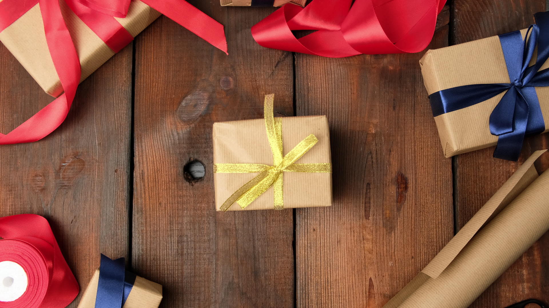 用棕色牛皮纸包装的礼物用丝带绑在棕色木桌上女人把盒子放在手里视频的预览图